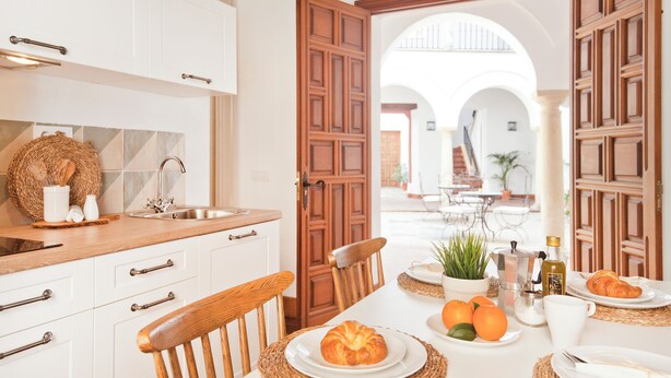 Eine moderne Küche mit weißen Schränken, einem Holzespeisetisch, der für das Frühstück gedeckt ist, und freiem Blick auf eine Terrasse.