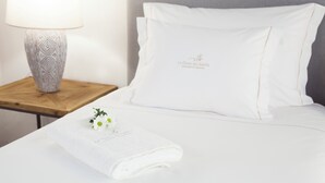 Ein ordentlich bezogenes Bett mit einem weißen Kopfkissen und einem gefalteten Handtuch mit floralem Muster.