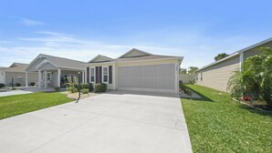 A single-story residential house with a front garage, a covered driveway, and a well-maintained lawn. - The Sunshine Retreat in the Villages with Golf Car (The Villages)