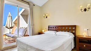 A hotel room with a large bed, a wooden headboard, two bedside tables with lamps, and a view of an outdoor seating area with umbrellas. - Marysol 32 - Penthouse in Benalmádena with swimming pool, 2 terraces, garage (Benalmádena)