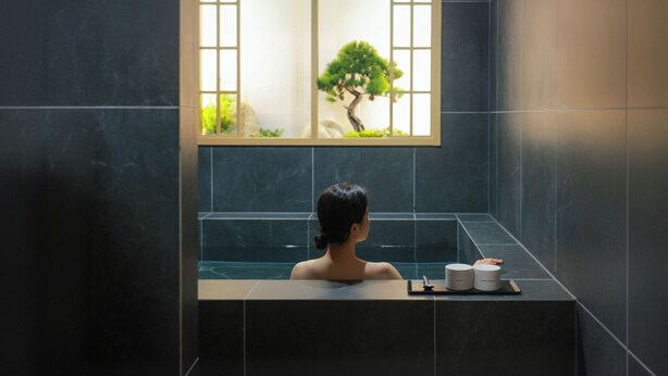 Una persona en una bañera con vistas a un árbol por la ventana.