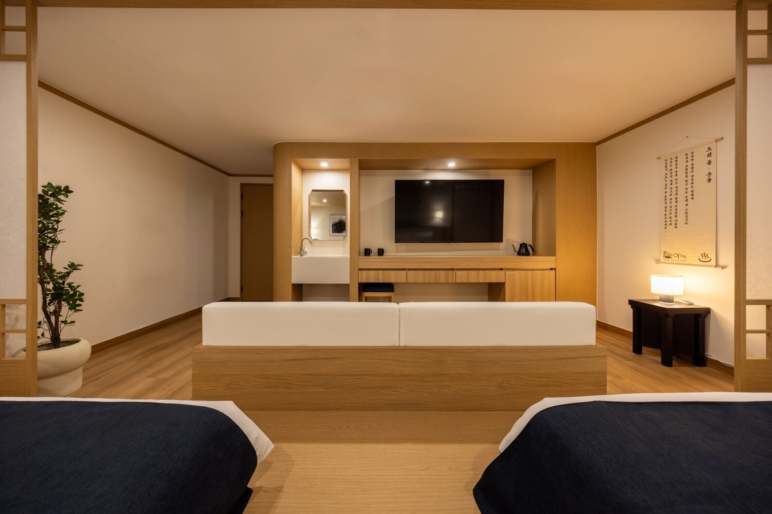 A hotel room with a large bed, a TV, a small sink, and a bedside table with a lamp.