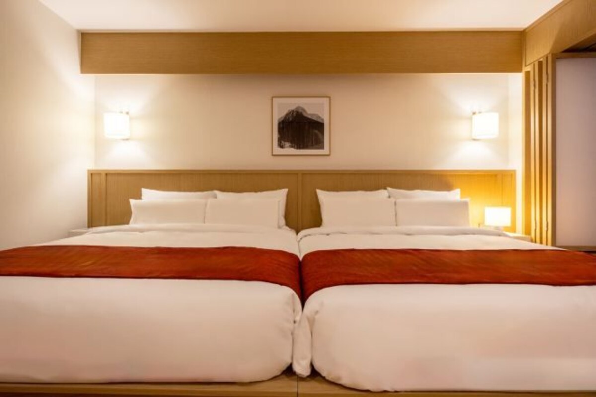 Una cama doble con dos almohadas y una colcha roja, un cabecero de madera y un cuadro enmarcado en la pared.