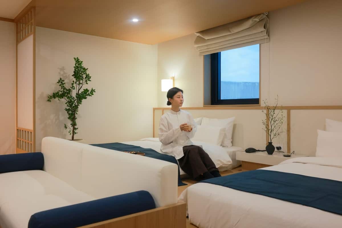 A hotel room with two beds, a sofa, a potted plant, and a window with a view.