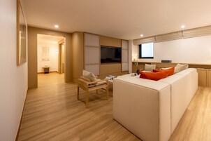 Quarto de hotel moderno com sofá, uma mesinha, televisão e janela.
