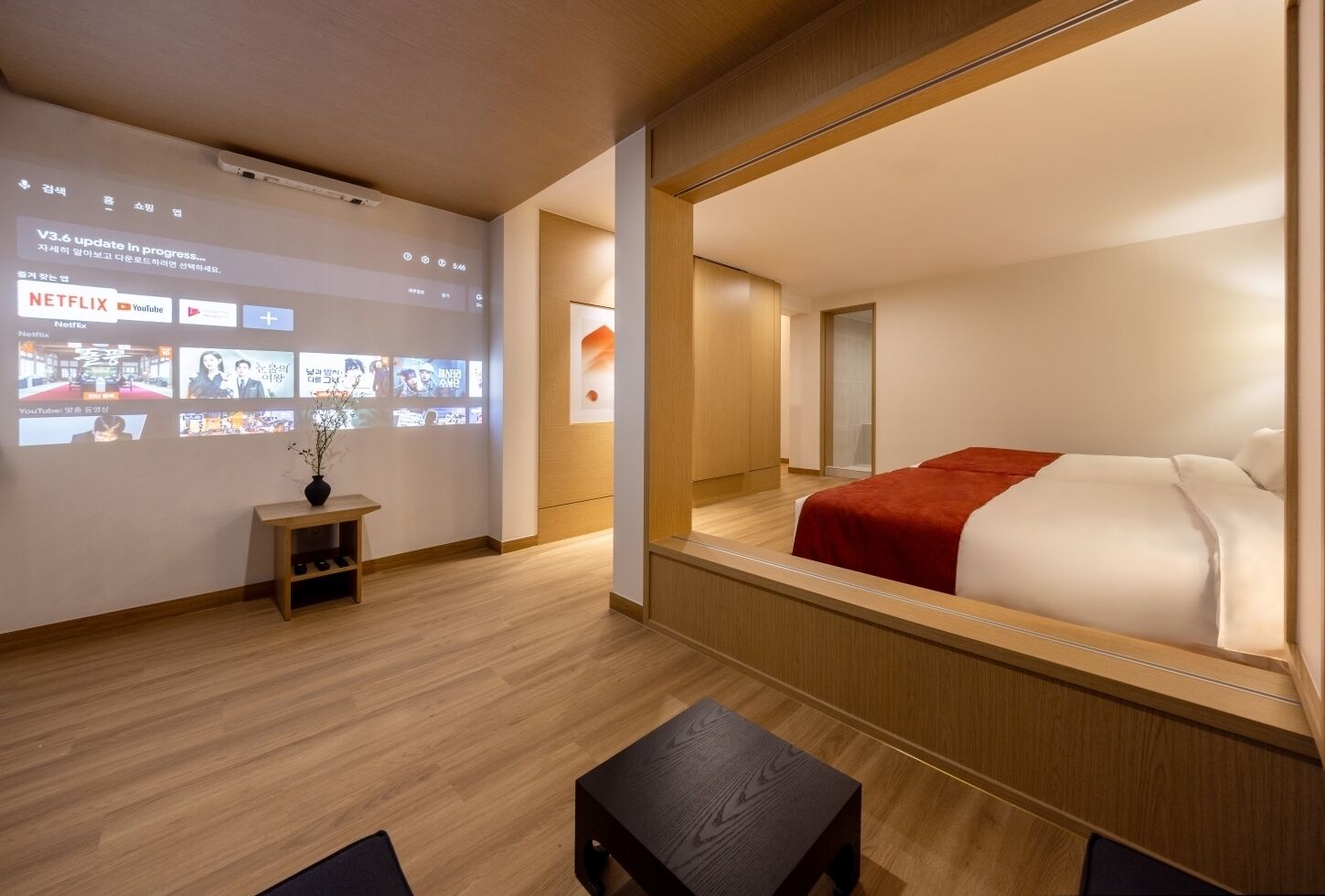 Habitación de hotel moderna con una cama grande, una mesita pequeña, una mesita de noche y un televisor empotrado que muestra servicios de streaming.