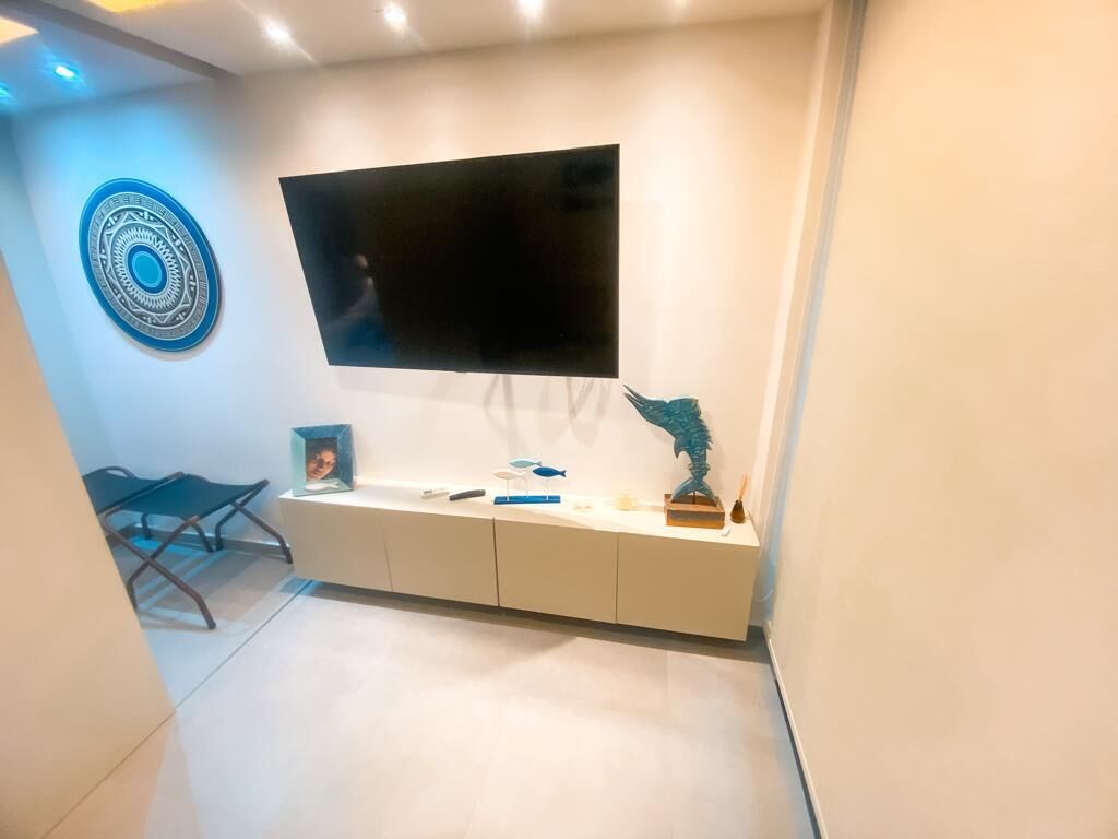 Uma sala de estar moderna com uma televisão de tela plana na parede, uma mesa de console branca com objetos decorativos e uma obra de arte circular azul na parede.