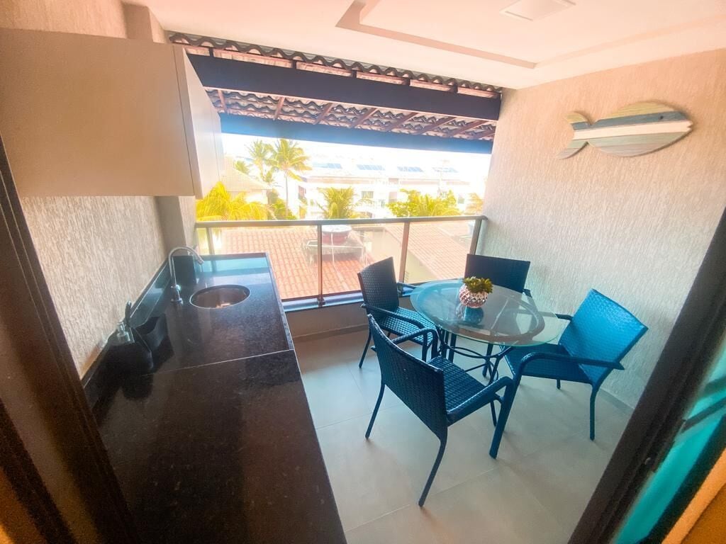 A balcony with a glass table and blue chairs, a small trash bin, and a decorative fish wall art piece.