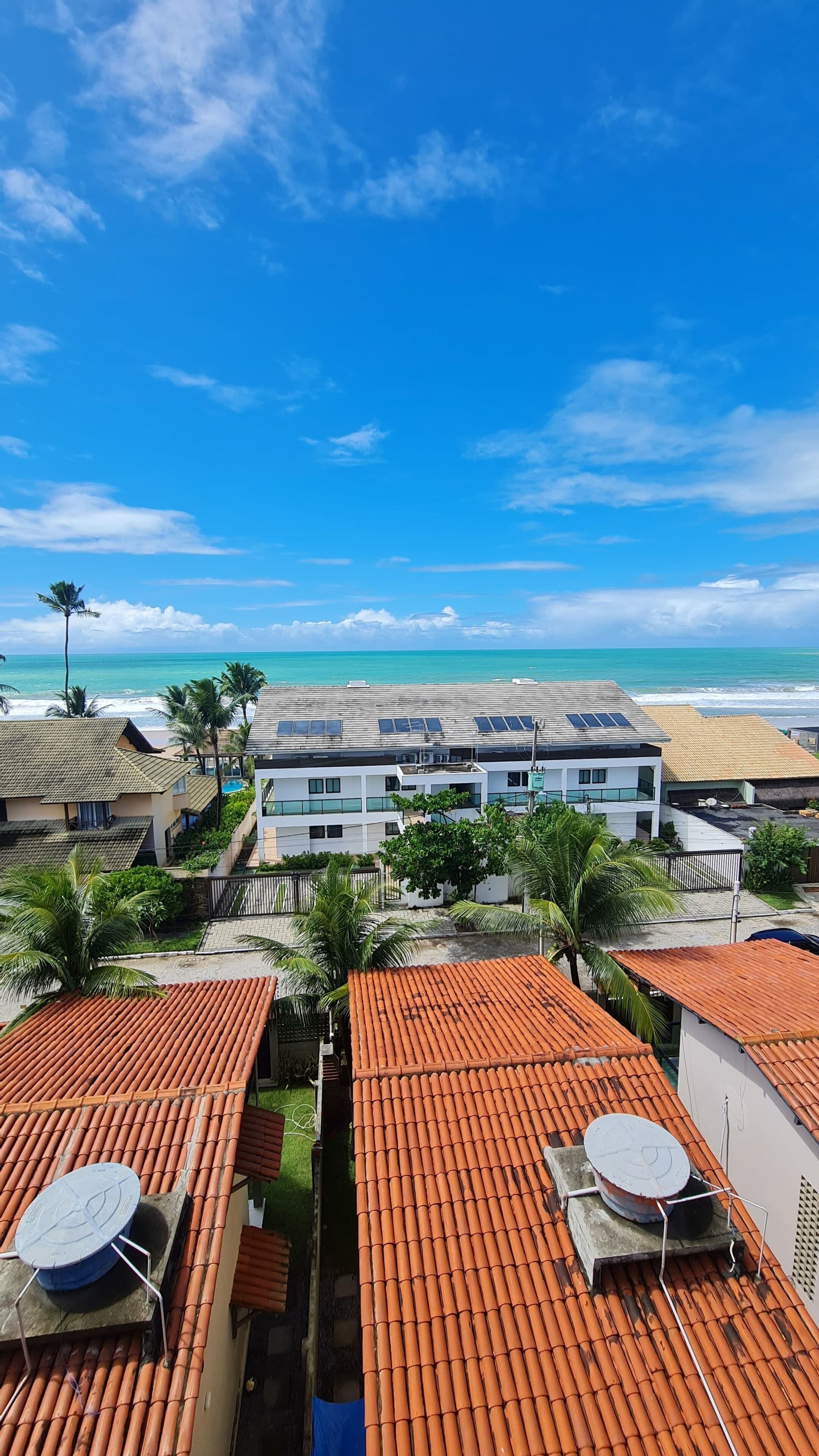 Uma área residencial costeira com telhados de terracota, painéis solares e vista para o oceano.