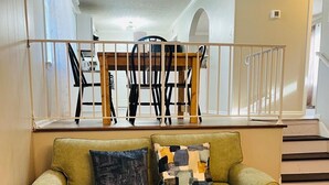 Una sala de estar con un sofá, dos cojines, una mesa de comedor con sillas y una escalera.