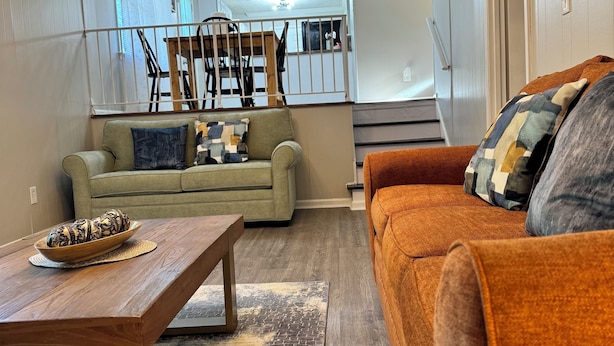 Un salón con sofá, una mesita de centro y un cuenco decorativo. Se ve una escalera en el fondo que sube a otra habitación.
