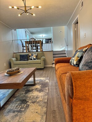 A living room with a sofa, coffee table, and a decorative bowl. There is a staircase in the background leading to another room. - Discover tranquility near Stone Mountain Park (Lilburn)