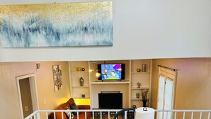 Un comedor con una mesa de madera, sillas negras y un televisor montado en la pared.
