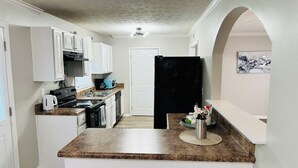 Una cocina compacta con armarios blancos, un refrigerador negro, un microondas y una cafetera sobre la encimera.