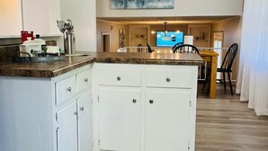 Una cocina con armarios blancos, encimera de granito y comedor con mesa y sillas de madera.