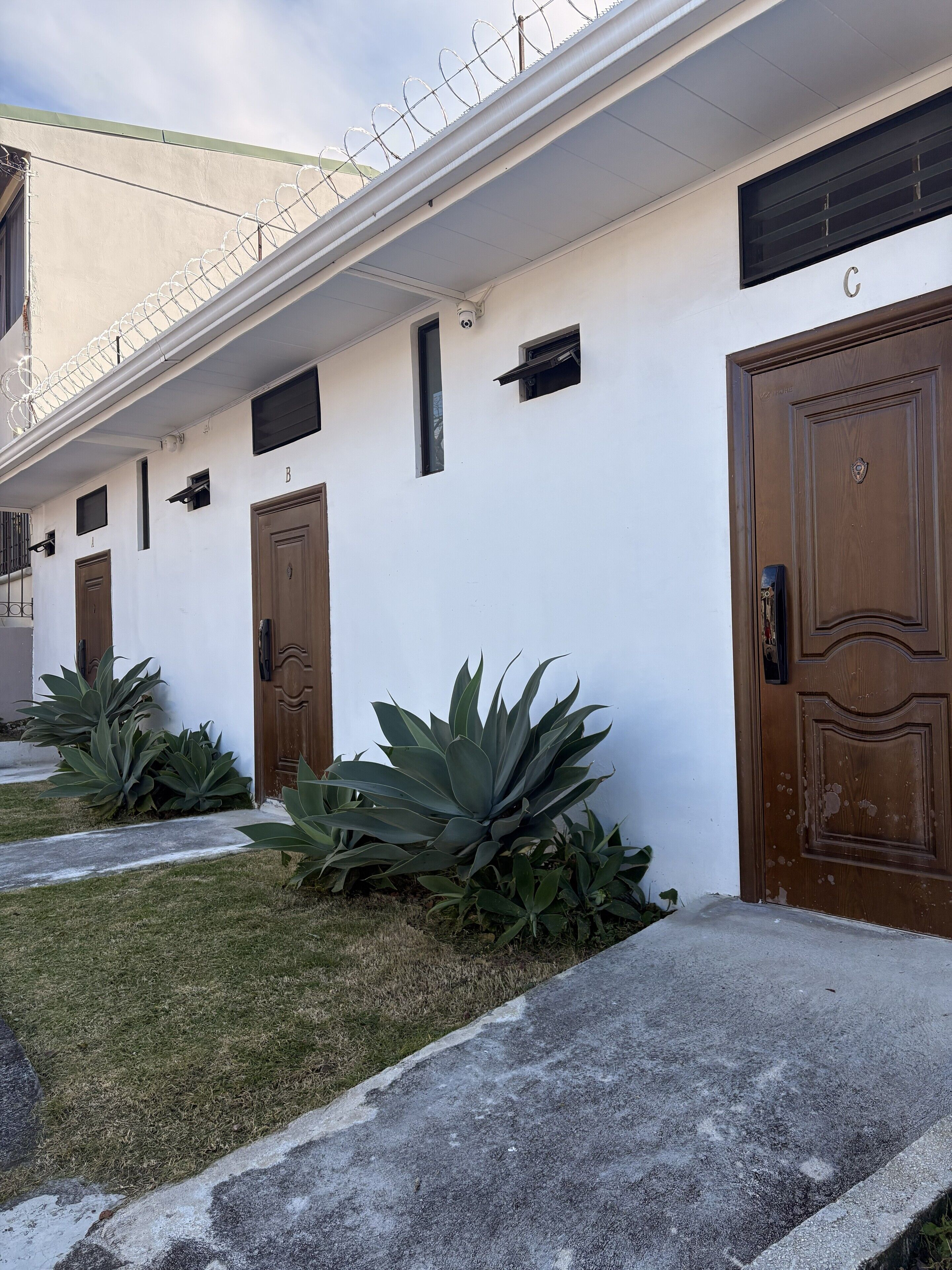 A row of white-walled buildings with brown doors, each marked with a letter.
