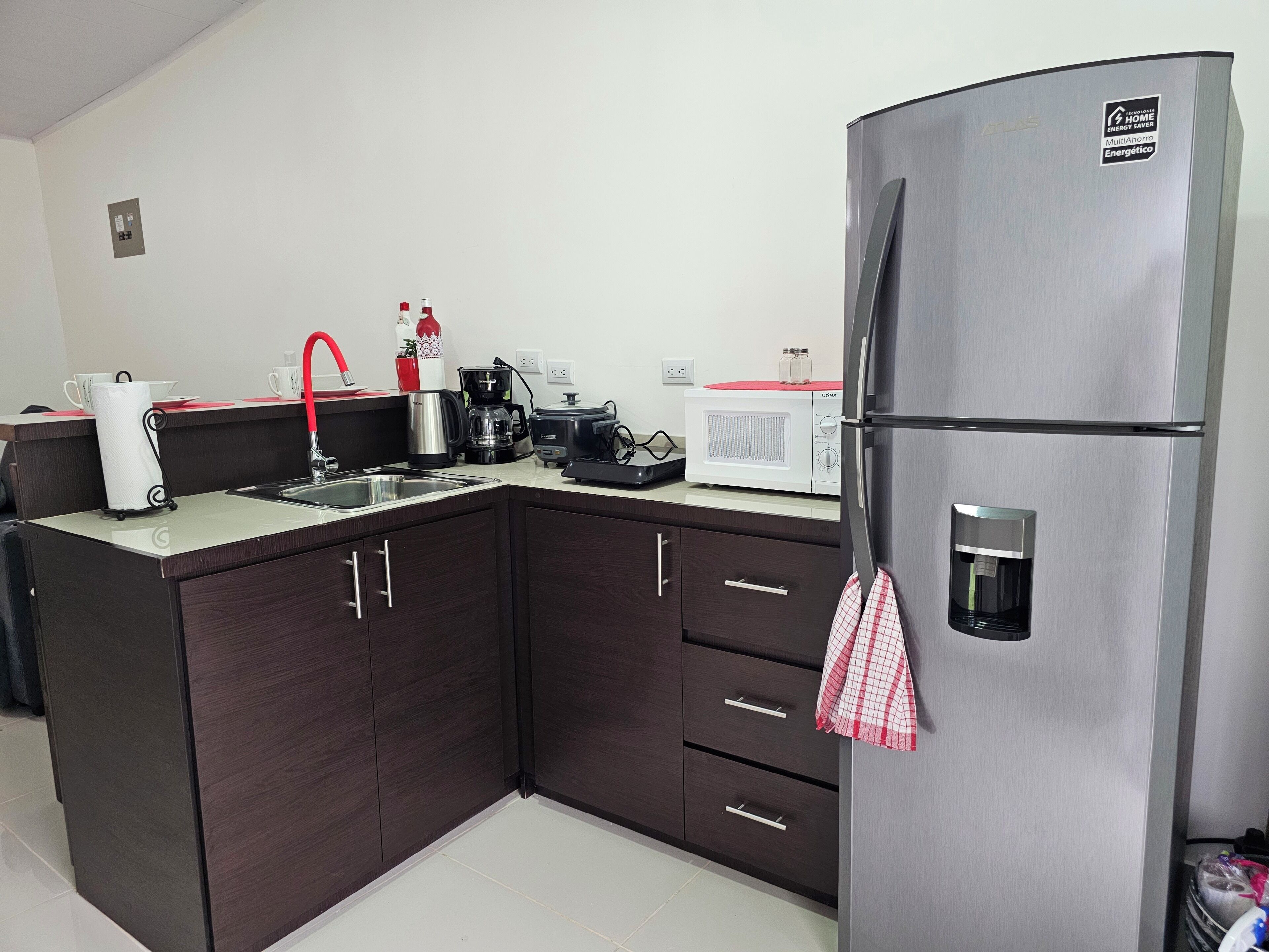 Une cuisine moderne avec des meubles de couleur sombre, un réfrigérateur en acier inoxydable, un four à micro-ondes, une machine à café et une bouilloire.