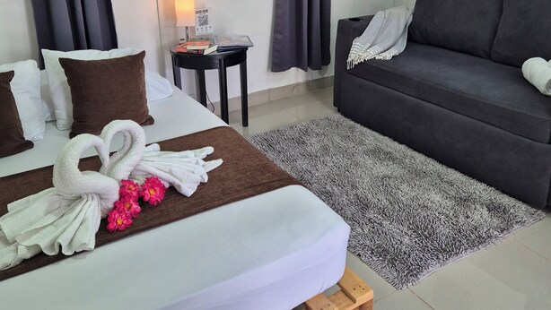 A hotel room with a bed, a sofa, a small table with a lamp, and a window with curtains.