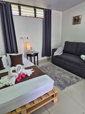 A hotel room with a bed, a sofa, a small table with a lamp, and a window with curtains. - BnB Eco Stay (San José)