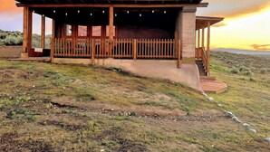 Een rustiek openluchtpaviljoen met een overdekte zithoek, een schoorsteen en uitzicht op het omliggende landschap.