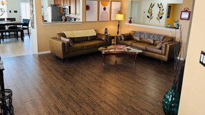 A living room with a brown leather sectional sofa, a glass coffee table, and a dining area with a wooden table and chairs. - Three bedroom home, pets allowed.  (Cypress)