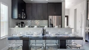 Cocina moderna con armarios oscuros, un refrigerador de acero inoxidable y una isla central con taburetes de bar.