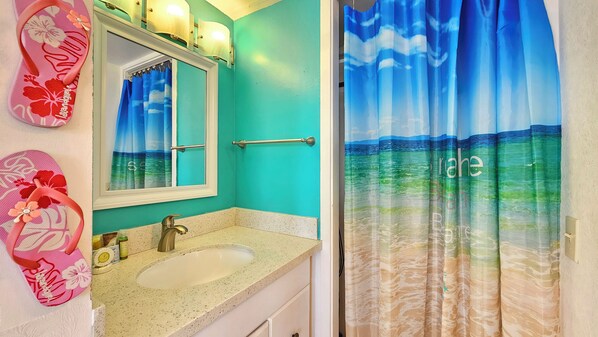 A bathroom with a turquoise wall, a sink, a mirror, and a shower curtain depicting a beach scene. - 15th Floor Central Waikiki Studio with Pool, Sleeps 3 (Honolulu)