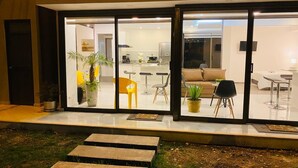 Una casa moderna amb una entrada amb porta de vidre, una cuina amb tamboretes de bar, una zona de menjador amb taula i cadires, i un saló amb sofà i taula de centre.