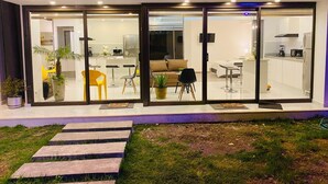 Una casa moderna amb façana de vidre, una zona de menjador i una cuina visibles a través de les portes de vidre.