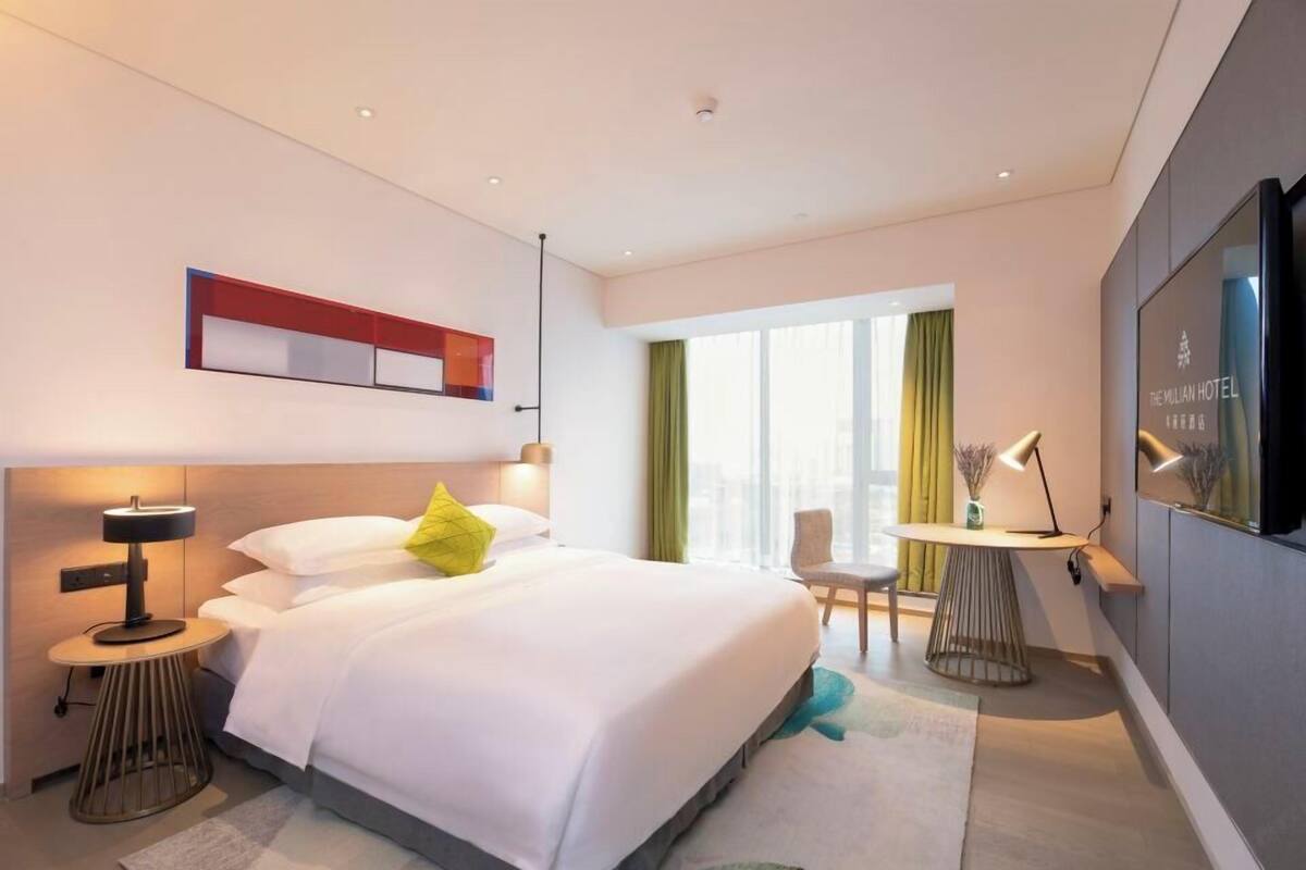A modern hotel room with a large bed, bedside tables, a desk, and a TV.