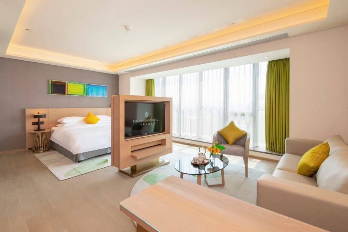 A hotel room with a bed, a TV, a sofa, a coffee table, and a window with curtains.