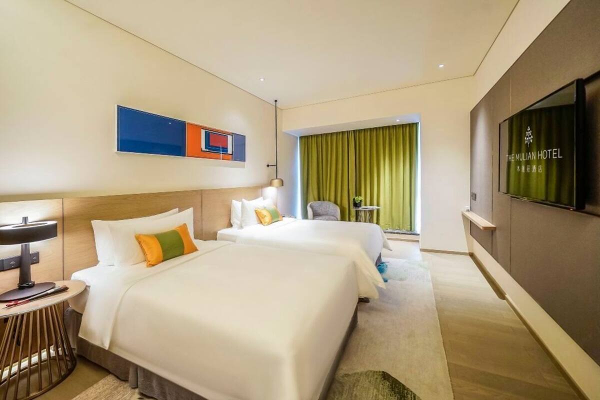 A hotel room with two beds, a TV, a desk, and a chair.