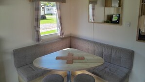 A corner room with a grey sofa, a small round table with a cross, and a window with curtains.