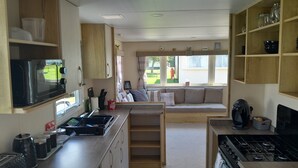 A compact kitchen with a stove, microwave, and sink. There is a seating area with a sofa and a window overlooking the yard.