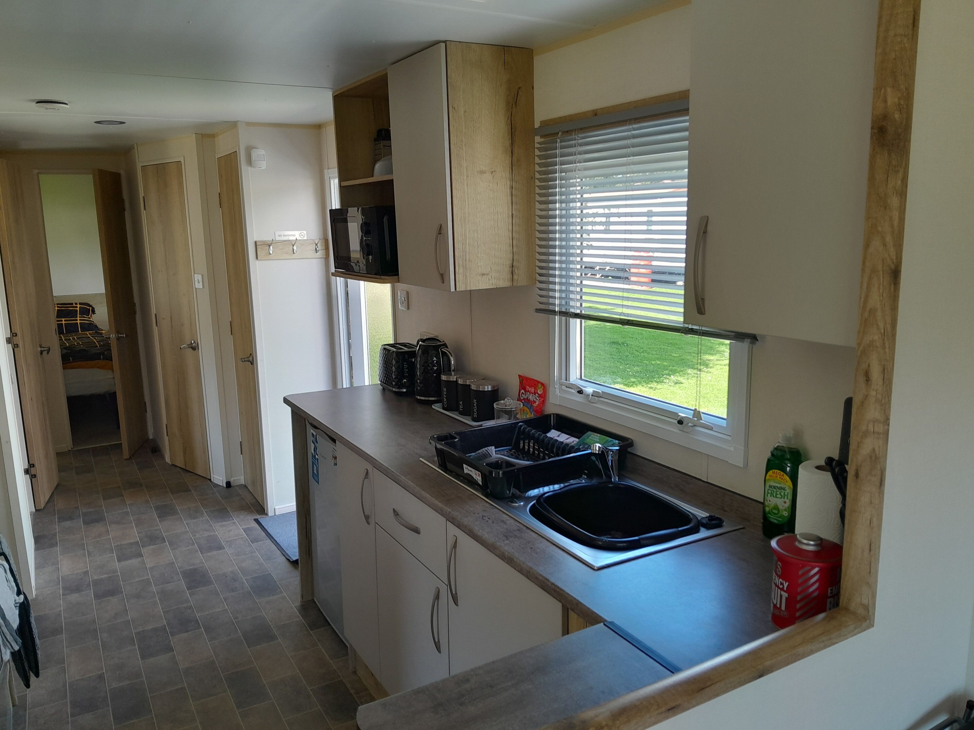 A compact kitchen with a built-in sink, wooden cabinets, and a window with blinds.