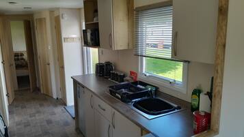 A compact kitchen with a built-in sink, wooden cabinets, and a window with blinds.