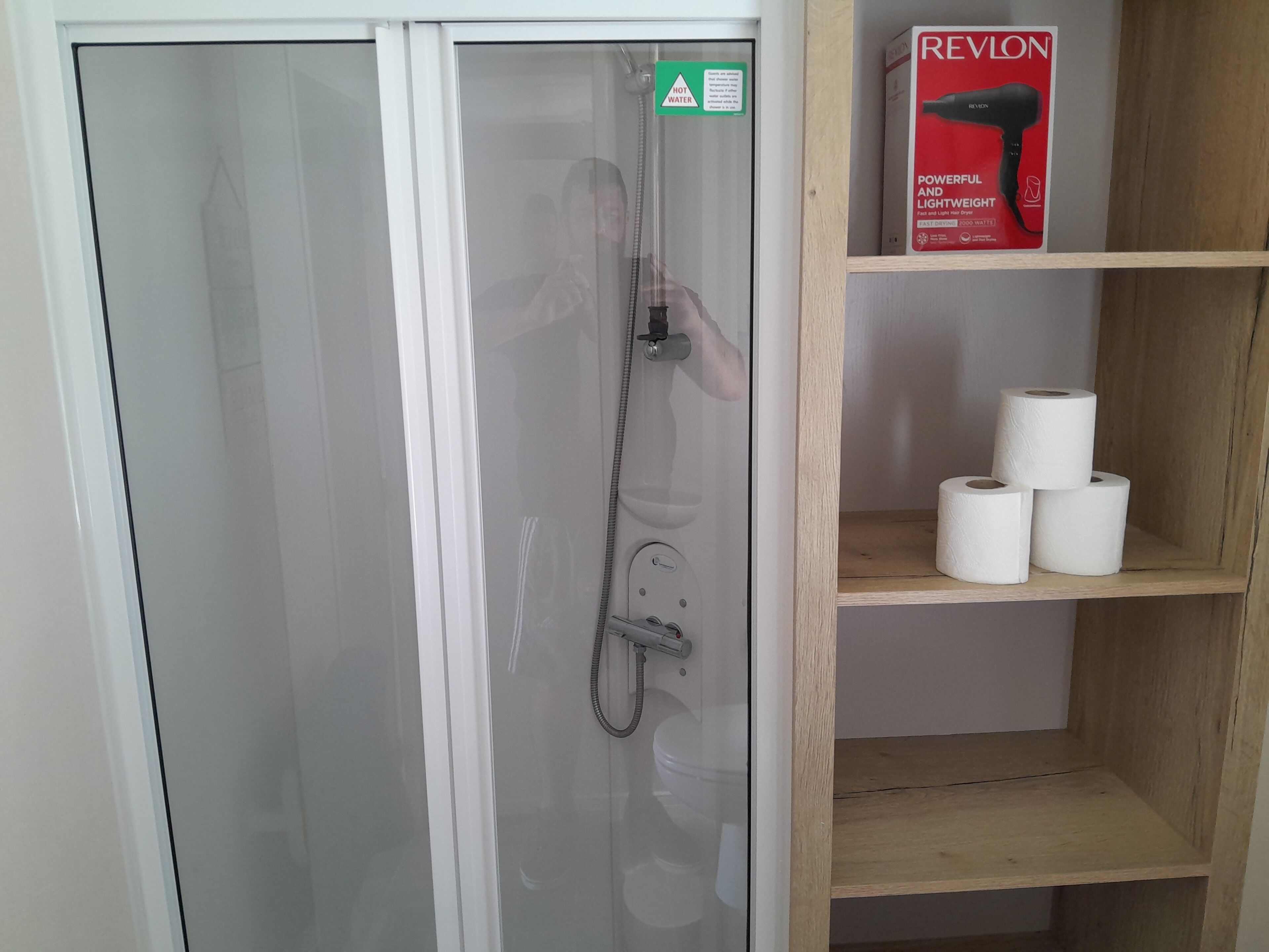 A shower enclosure with a frosted glass door, a handheld showerhead, and a shelf with toilet paper.