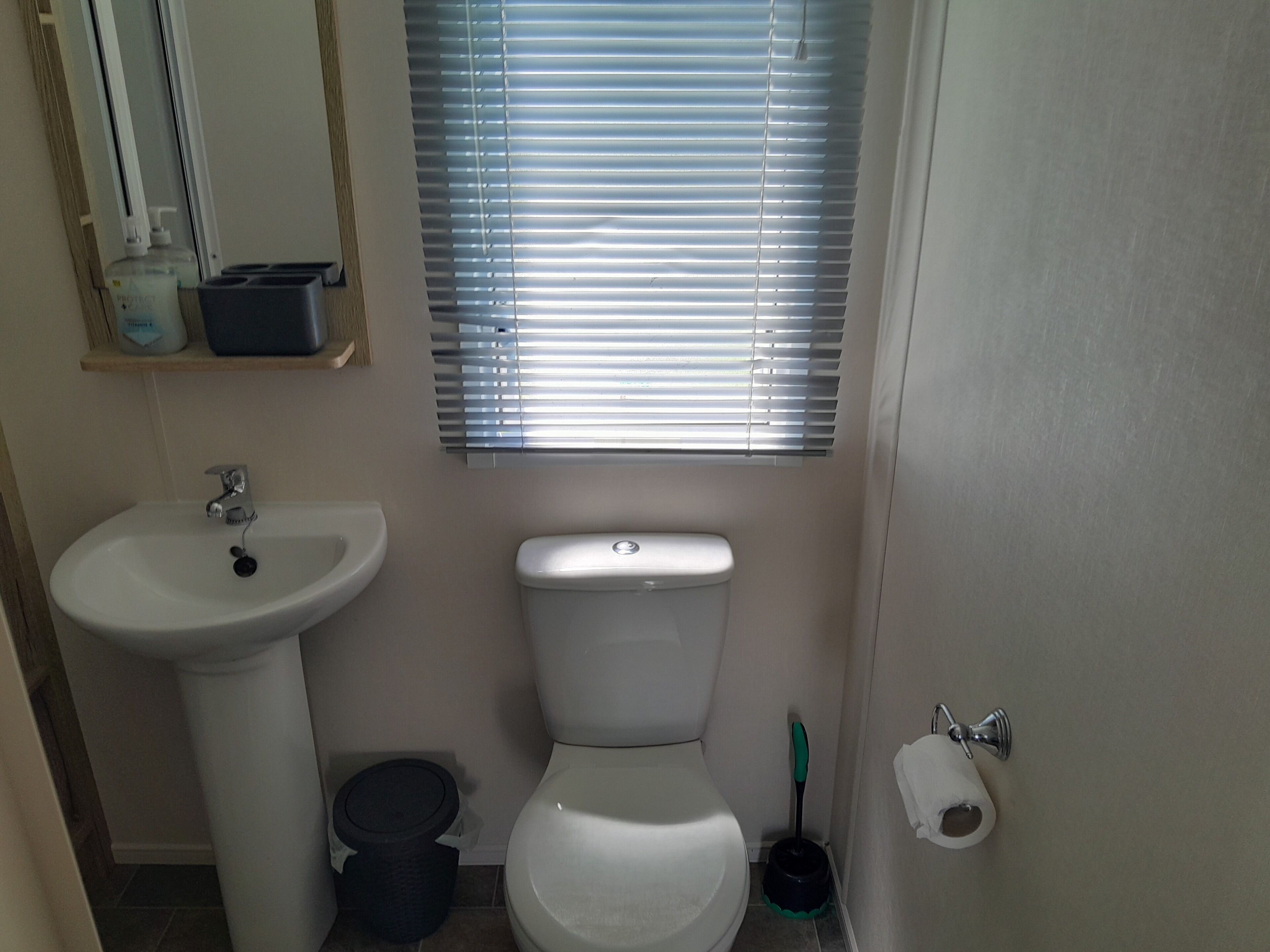 Une petite salle de bain avec un lavabo, des toilettes et des stores aux fenêtres.