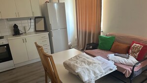 Un espace de vie compact comprenant un coin cuisine, une table à manger avec des chaises, un canapé avec des coussins et un lit.