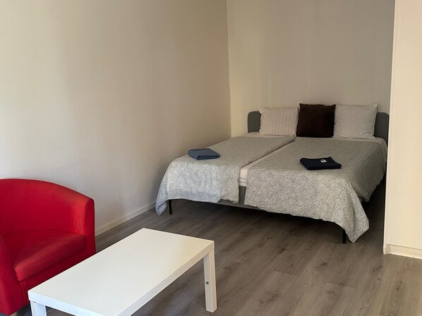 Een kleine, verzorgde kamer met een bed, een rode stoel en een witte tafel.