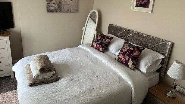 A neatly made bed with white linens and decorative pillows, a bedside lamp, and artwork on the walls.