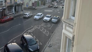 A street view with parked cars, buildings, and a pedestrian.