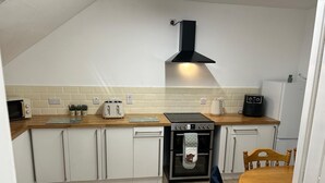 A compact kitchen with white cabinets, a black stove, and a wooden dining table.
