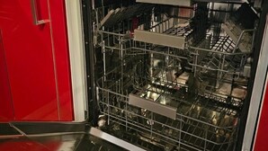 En åben opvaskemaskine med hylder og bestik indeni, et rødt skab og en kaffemaskine på bordpladen.