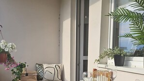En balkon med et træbord dækket til to personer, en hængende plante og en sofa med puder.