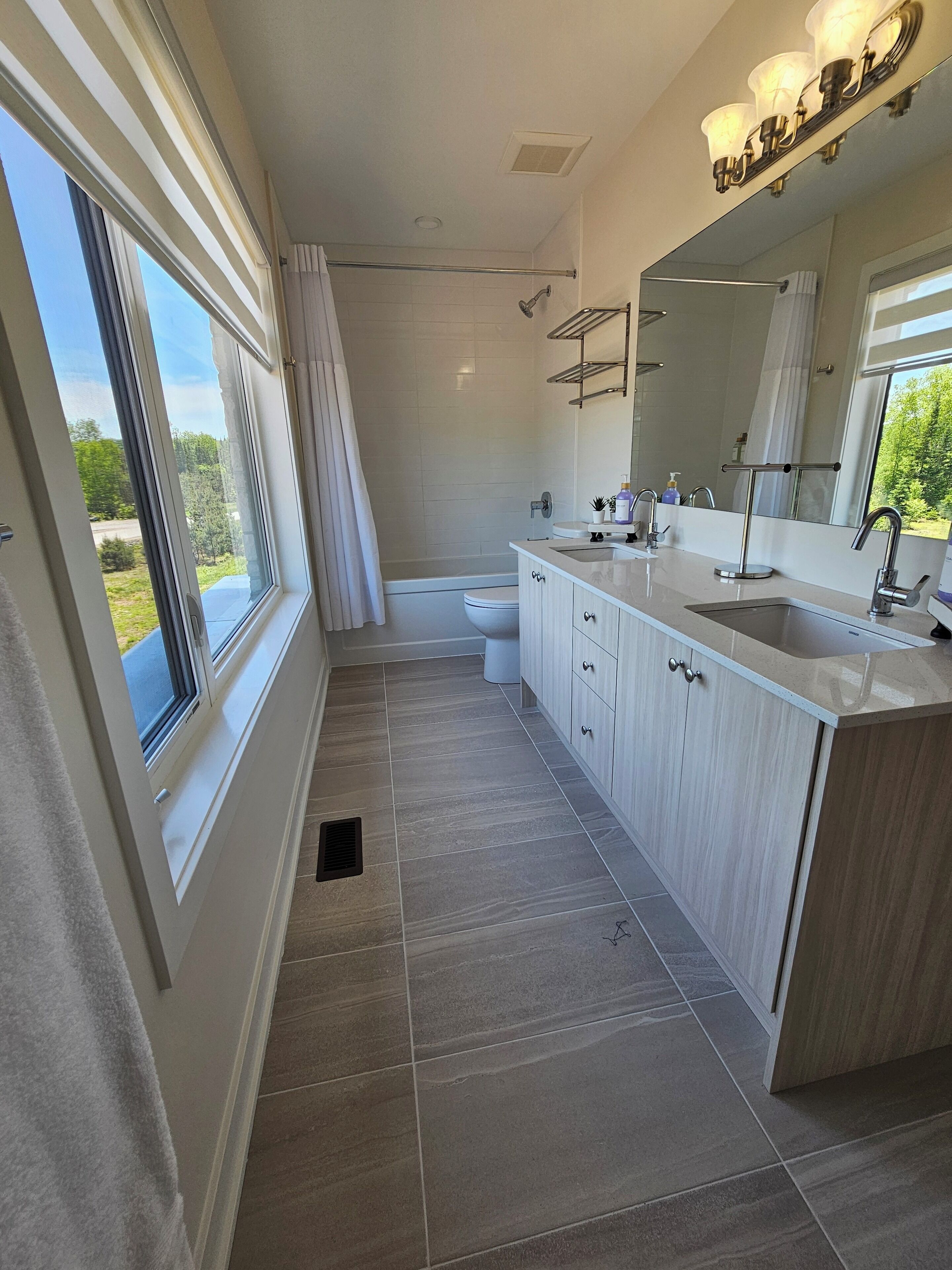 Une salle de bain moderne dotée d’une grande fenêtre, d’une baignoire, d’une douche et d’un meuble-lavabo avec un miroir.