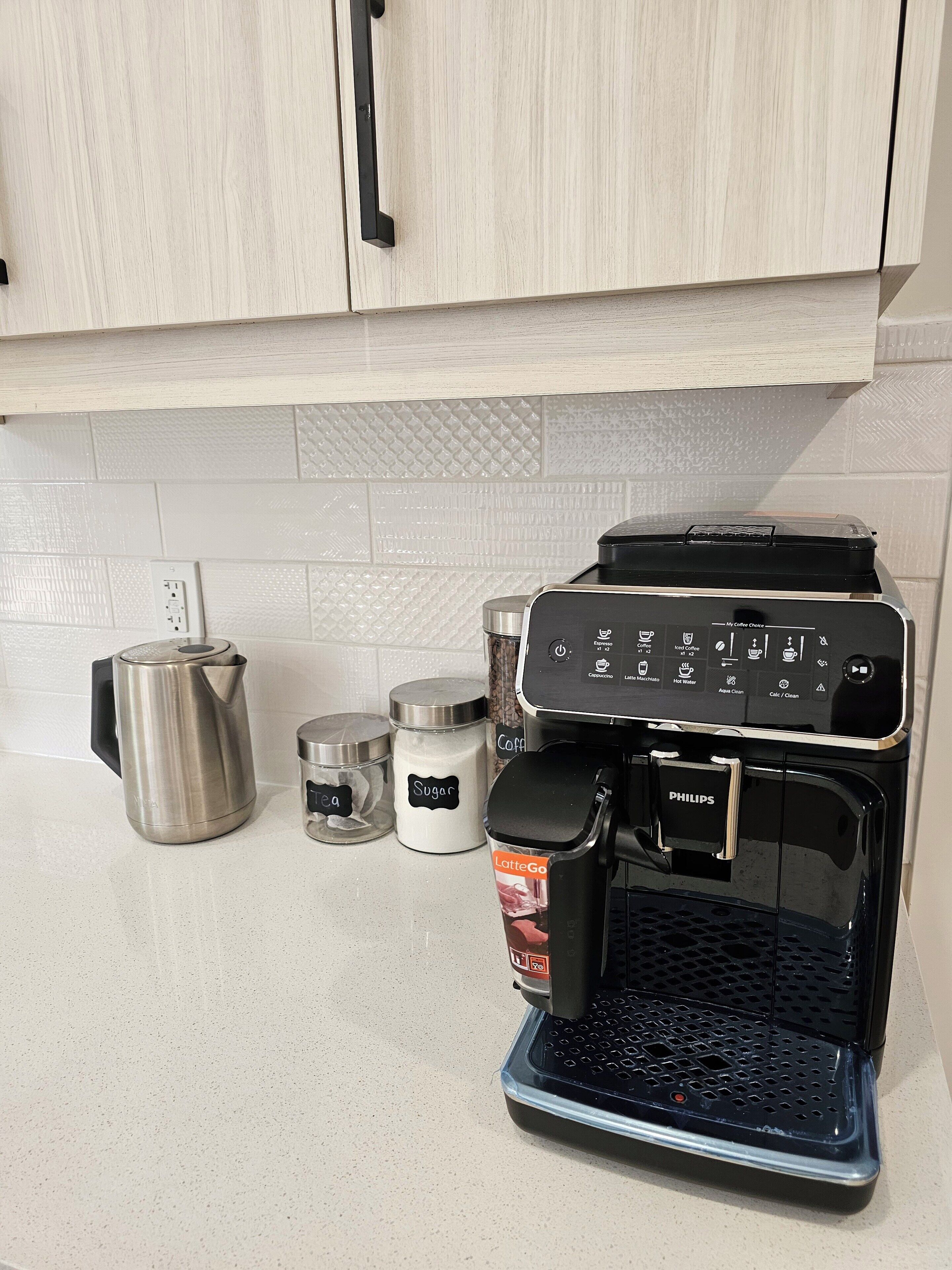 Una cafetera con espumador de leche y un soporte para cápsulas de café sobre una encimera de cocina.