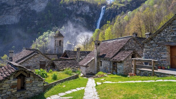 Un pueblo de piedra con arquitectura tradicional, un camino de piedra y una cascada al fondo.