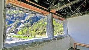 Una habitación con vista a un paisaje montañoso, un banco de piedra y un techo de madera rústica.