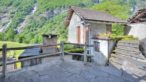 Un edificio rústico de piedra con una escalera de madera y barandilla metálica, con vistas a un exuberante valle verde y una cascada.